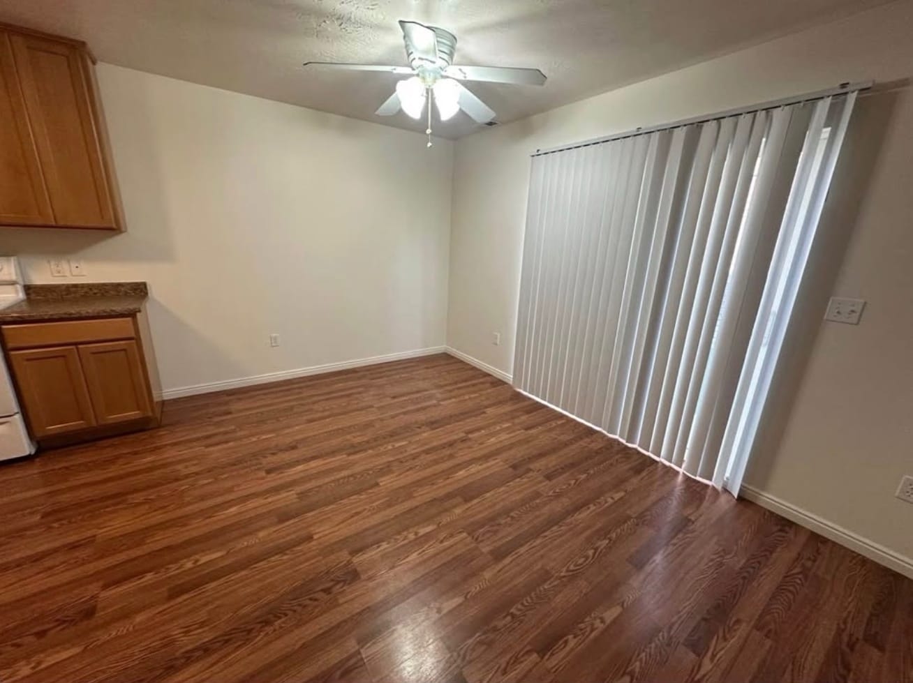 Dining area next to the kitchen, with wood-look flooring, a ceiling fan and a sliding glass door behind vertical blinds