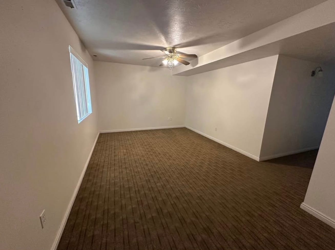 A large carpeted room with a ceiling fan and a window along one wall