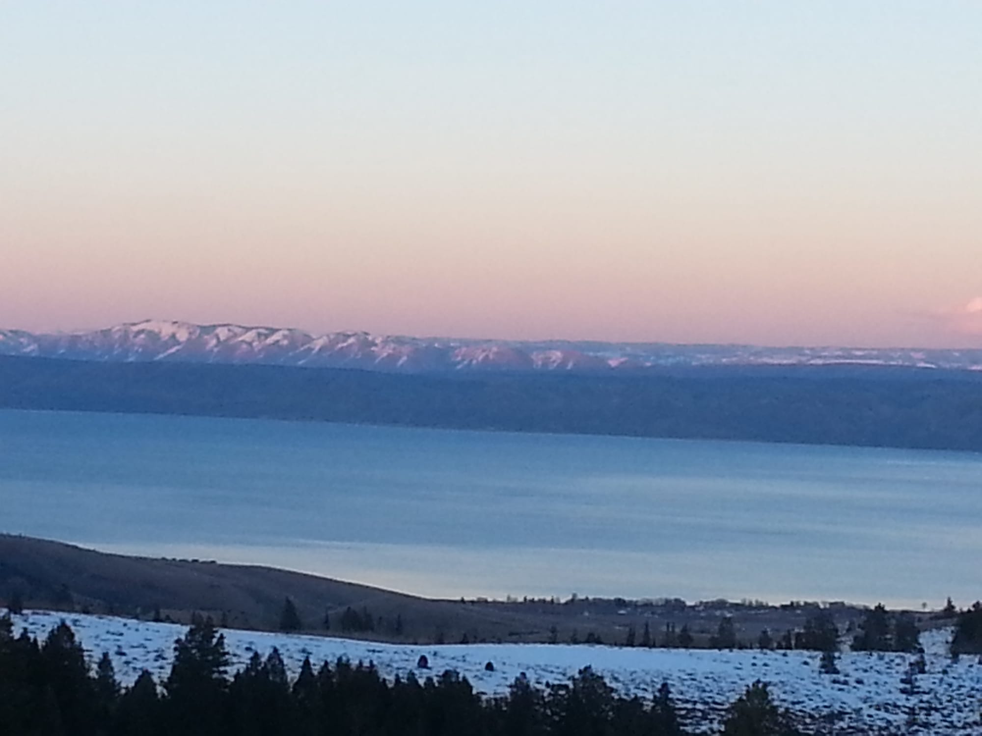 Bear Lake in winter at dusk, with snow on the hills in the foreground and on the mountains across the water