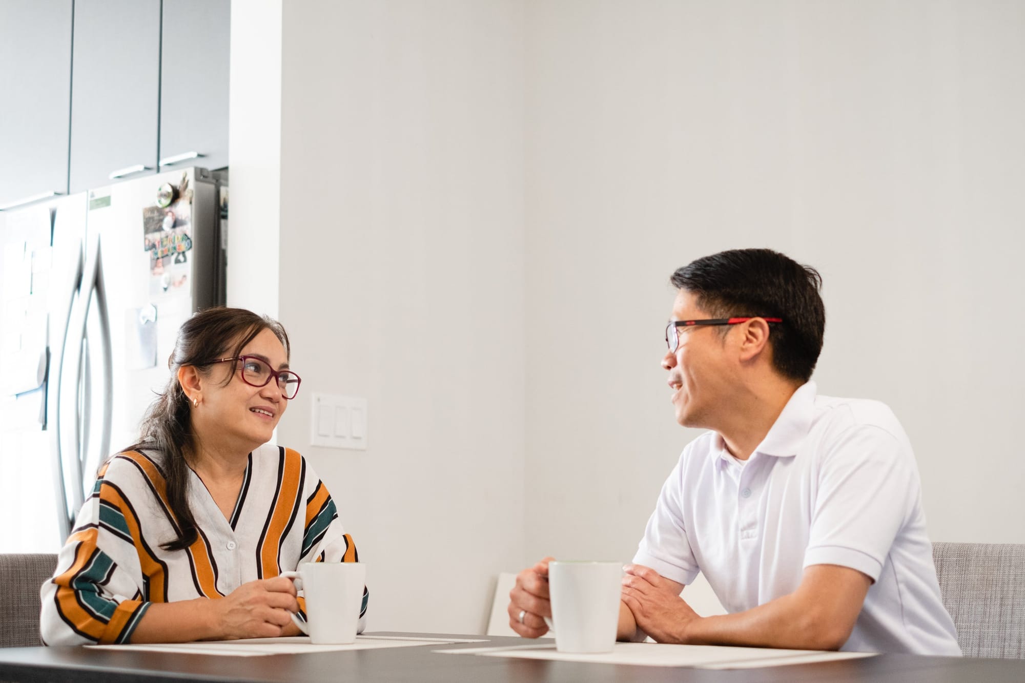 Two people talking over mugs of tea at a kitchen table