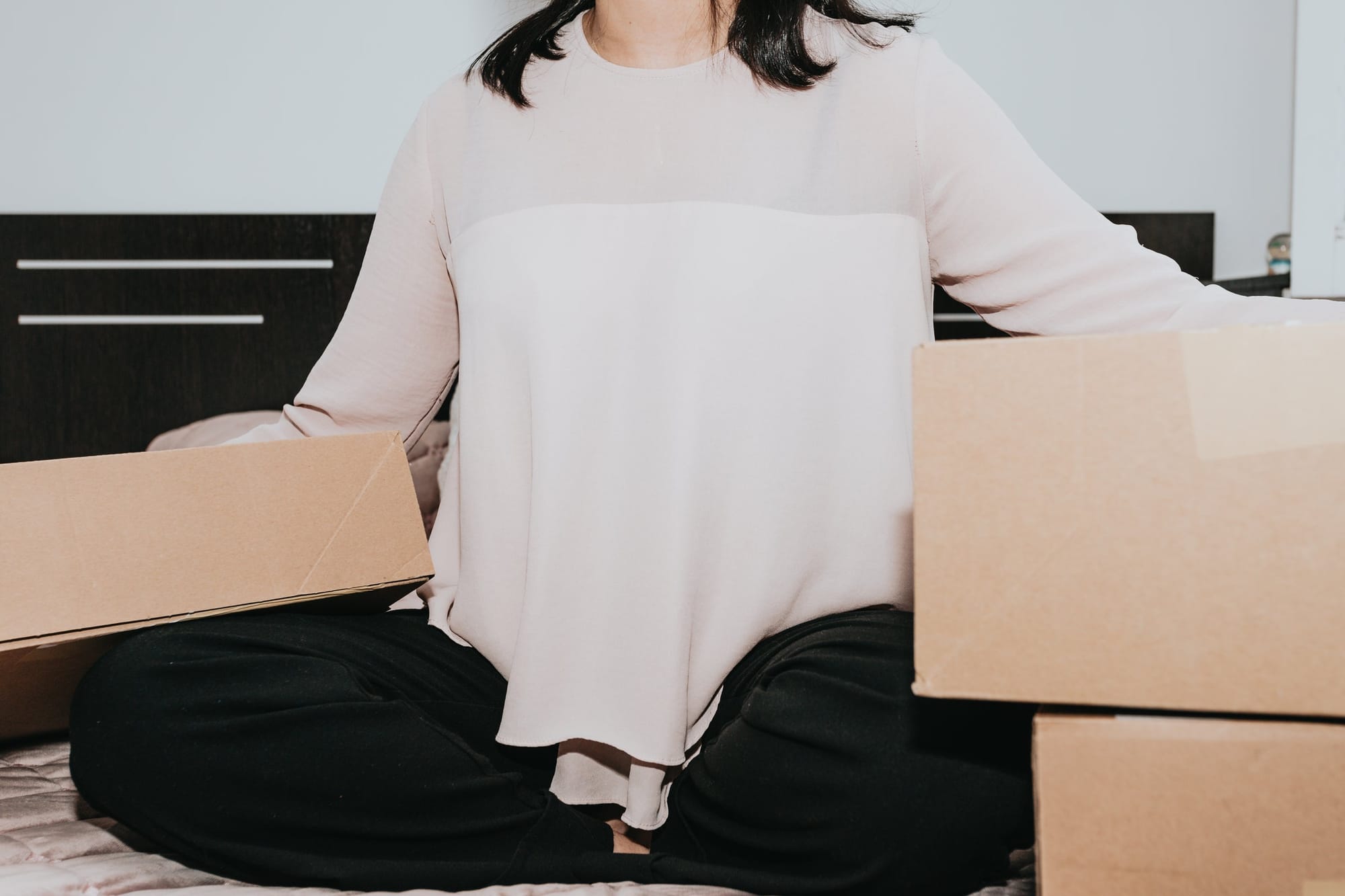 A person sitting cross-legged on the floor among large cardboard boxes